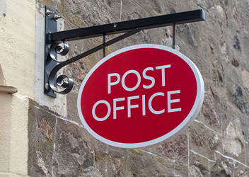 A red oval sign with white text reads 'Post Office,' mounted on a stone wall.